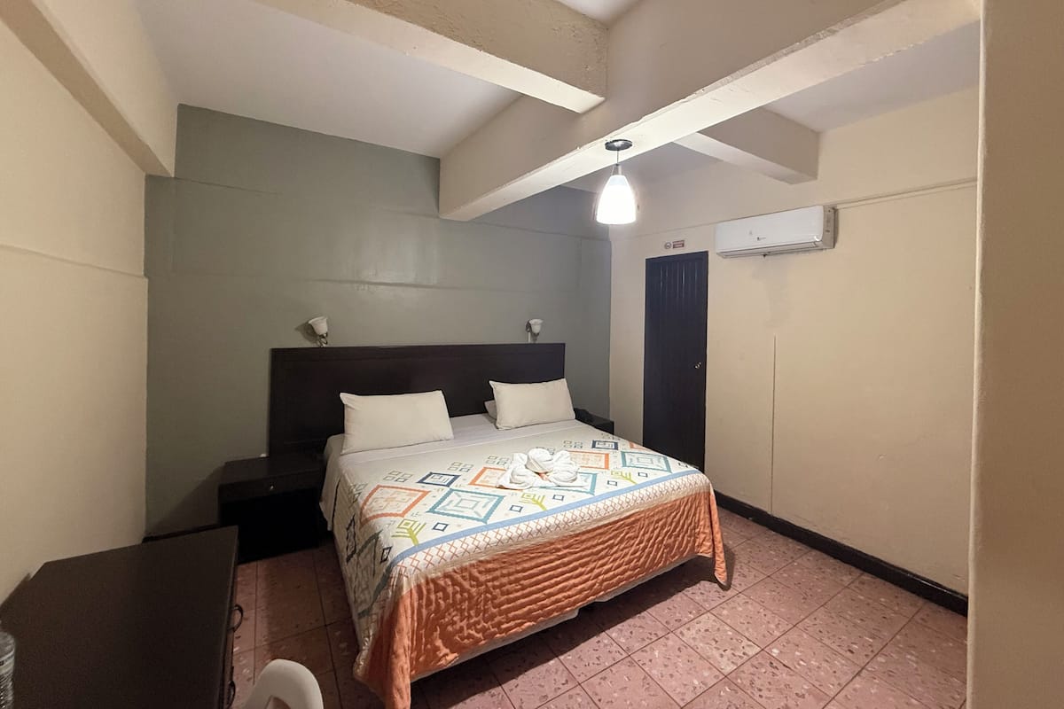 Un dormitorio con cama, mesitas de noche, ventilador de techo, aire acondicionado y una puerta.