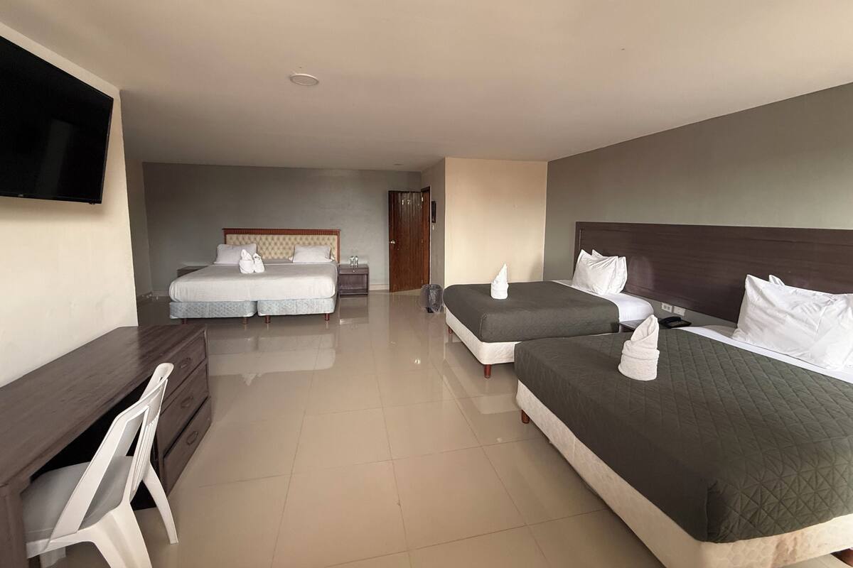 Habitación de hotel con dos camas, un escritorio, una silla, un televisor y una puerta.