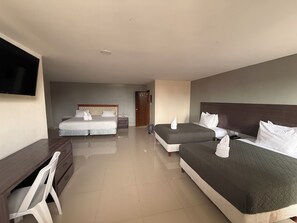 Ein Hotelzimmer mit zwei Betten, einem Schreibtisch, einem Sessel, einem Fernseher und einer Tür.