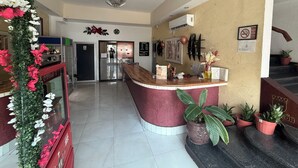 A reception area with a counter, a Coca-Cola refrigerator, a clock, and a staircase with potted plants. - EL BARON HOTEL (Tapachula)