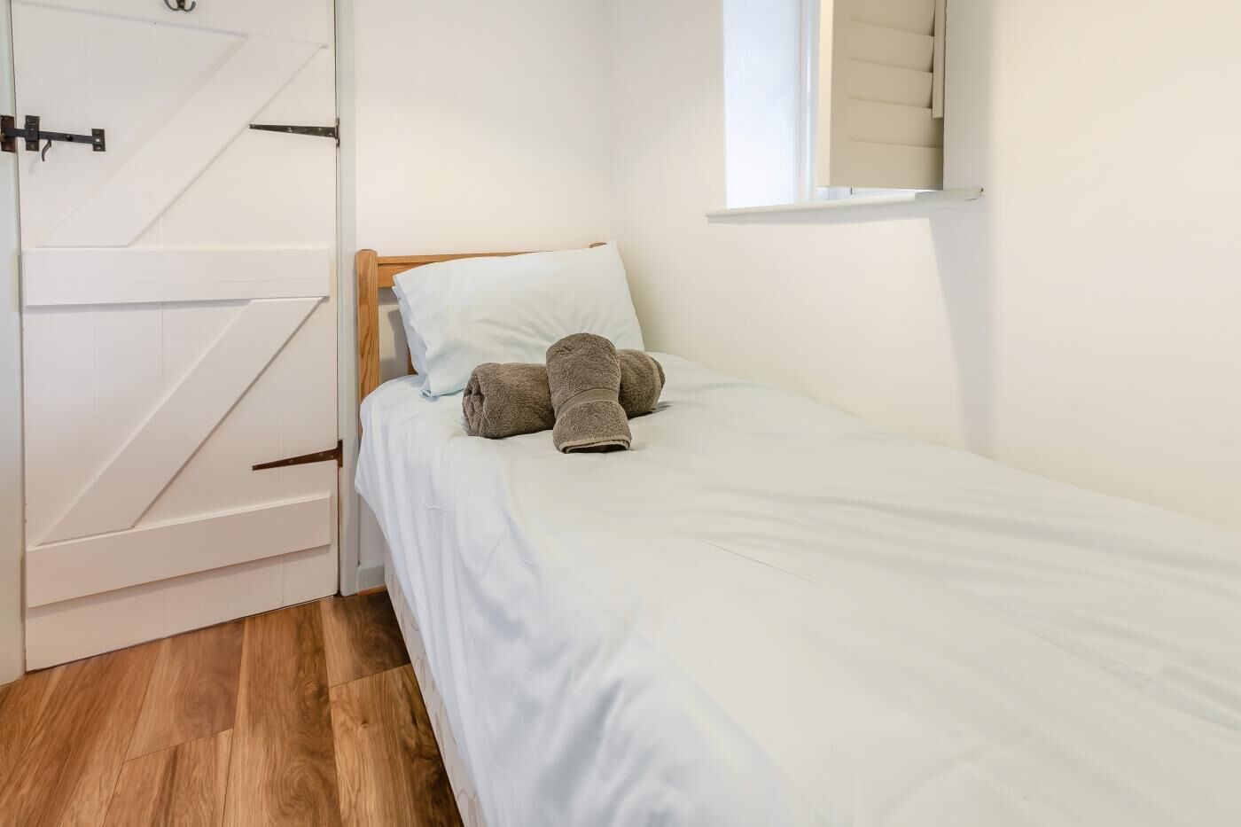 A small, neatly made bed with a wooden headboard, a white pillow, and two folded towels.