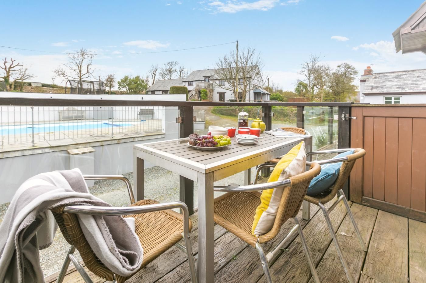 A balcony with a table set for breakfast, wicker chairs, and a view of a swimming pool.