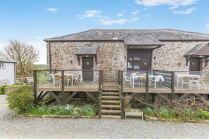 Ein Steinhaus mit Holzterrasse, Sitzgelegenheiten im Freien und einer kleinen Treppe zum Eingang.