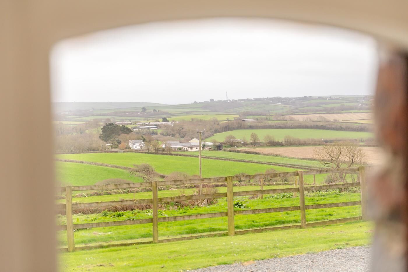 Un paysage rural avec des champs, une clôture en bois et un bâtiment situé au loin.