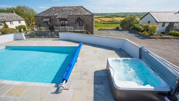 Une piscine avec un jacuzzi, des carreaux de pierre et un bâtiment en pierre en arrière-plan.