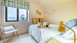 Un dormitorio con cama, mesita de noche, ventana con vistas, silla y lámpara de noche.