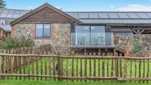 Un edificio de piedra con techo de madera, un invernadero de cristal y una valla de madera.
