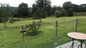 Una terraza con una mesa redonda y sillas, con vistas a una zona cubierta de césped, árboles y una valla.