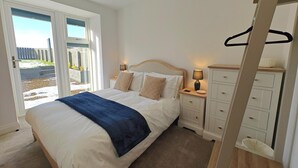 Un dormitorio con cama, mesitas de noche, cómoda y puerta corrediza de vidrio que da a un espacio exterior.