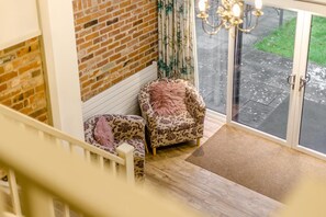 Una habitación con pared de ladrillo, dos sillones estampados, piso de madera y una puerta de vidrio que da al exterior.