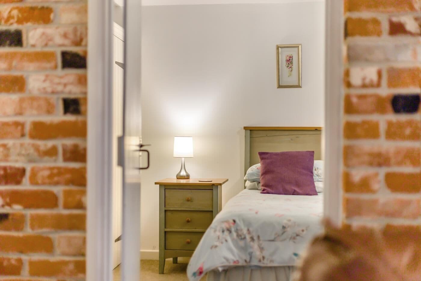 Ein Schlafzimmer mit Bett, Nachttisch, Lampe und einem gerahmten Bild an der Wand.
