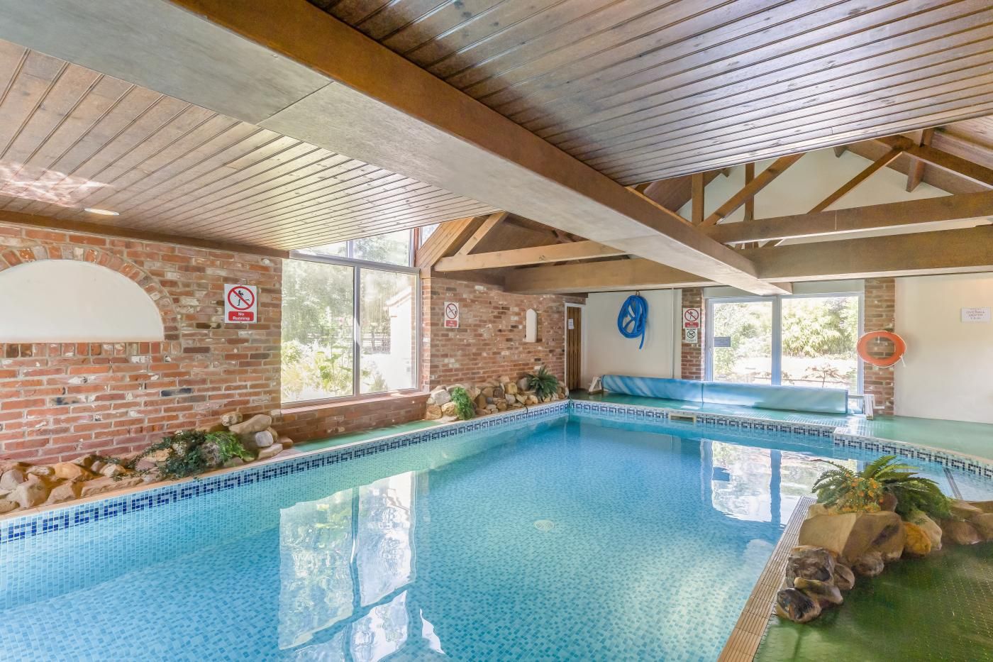 An indoor swimming pool with a tiled floor, brick walls, and wooden beams.