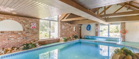 An indoor swimming pool with a tiled floor, brick walls, and wooden beams.