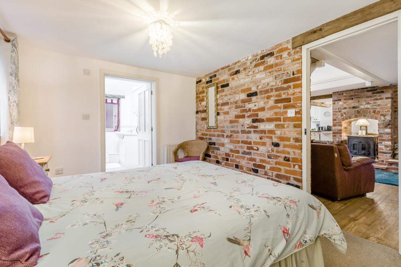 A bedroom with a brick wall, a bed with floral bedding, a chair, and a wooden floor.