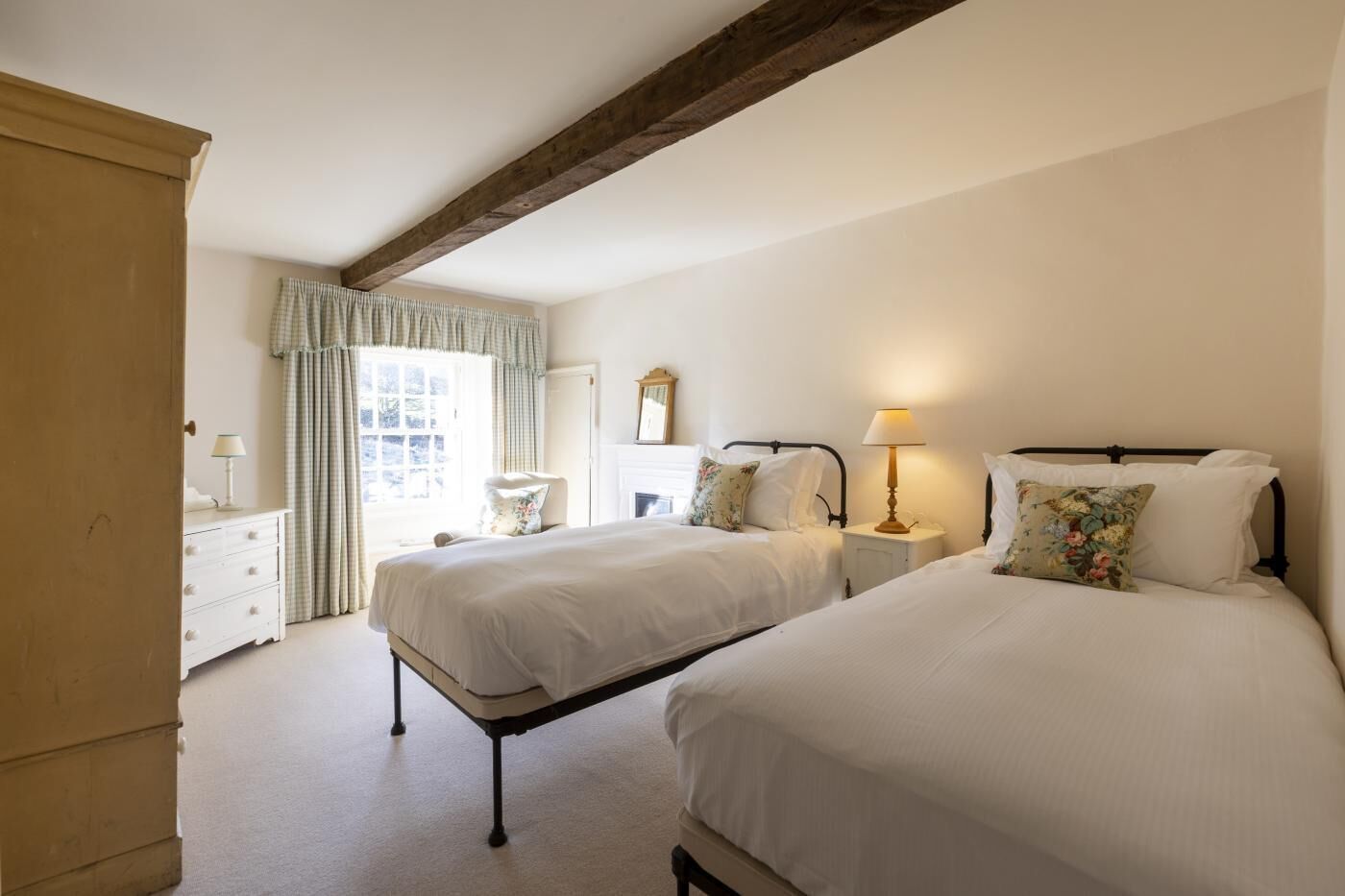 A bedroom with two beds, a dresser, a chair, and a window with curtains.