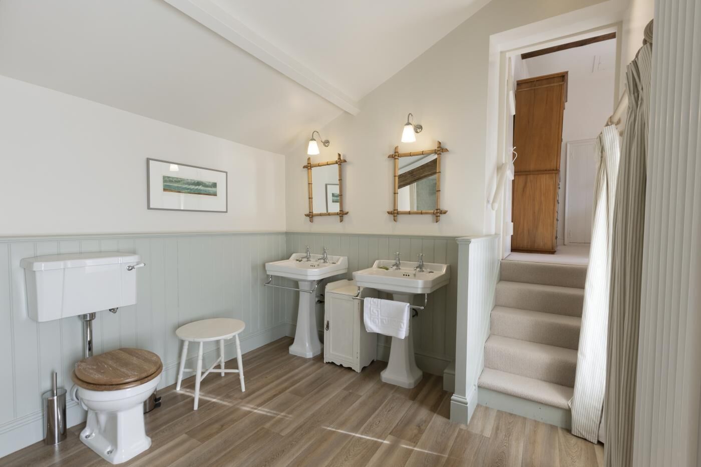 Een badkamer met toilet, twee wastafels, een spiegel en een trap naar een andere kamer.