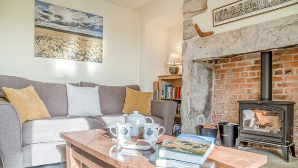 Ein Wohnzimmer mit einer Couch, einem Couchtisch mit Teekannen und einem Buch, einem Kamin und einem Bücherregal.
