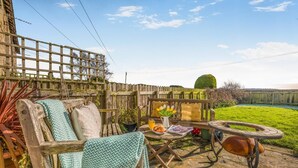 Eine Holzterrasse mit einer Bank, einem Tisch mit Getränken und Speisen sowie Blick auf einen Garten.