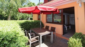 Un patio con una mesa y sillas, un paraguas rojo y un edificio con techo de tejas y ventanas.
