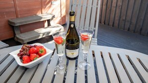 Pöydällä on pullo Prosecco-kuohuviiniä, kaksi lasia sekä kulho täynnä viinirypäleitä ja mansikoita.