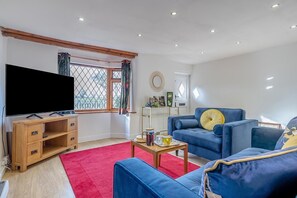 A living room with a TV, blue sofa, red rug, and a window with curtains. - 2 Bed in Hunningham (oc-h34740) (Hunningham)