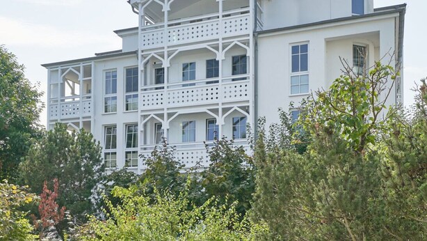 Een meerlaags gebouw met een witte gevel, meerdere balkons en een gebogen dakgedeelte.