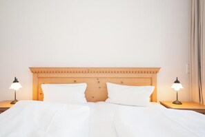 Ein Hotelzimmer mit einem hölzernen Kopfteil, zwei Nachttischlampen und einem ordentlich bezogenen Bett mit weißen Leinen.