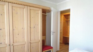 Een kamer met een houten garderobe, een rode stoel en een bed.