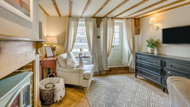 A cozy room with exposed wooden beams, a white sofa, a TV, and a fireplace. - 1 Bed in Holt (oc-p34797) (Holt)