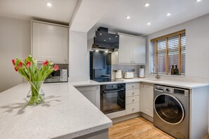 A modern kitchen with built-in appliances, a large window with blinds, and a vase of flowers on the counter. - 2 Bed in Dersingham (oc-o34800) (Dersingham)