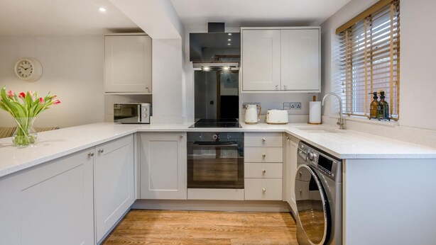 Een moderne keuken met witte kasten, een inbouwoven, een magnetron en een vaatwasser.