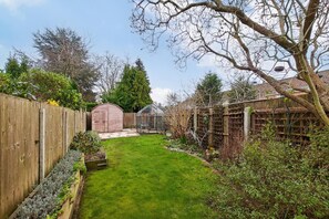A backyard with a wooden fence, a shed, a greenhouse, and a variety of plants. - 2 Bed in Dersingham (oc-o34800) (Dersingham)
