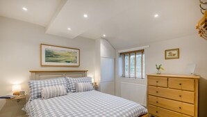 Een slaapkamer met een bed, een dressoir, een raam met jaloezieën, een radiator en een schilderij aan de muur.