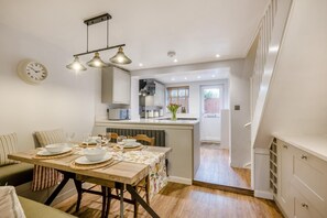 A modern kitchen with a dining area, featuring a wooden table set for a meal, pendant lighting, and a clock on the wall. - 2 Bed in Dersingham (oc-o34800) (Dersingham)