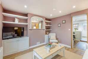 A modern living room with a sofa, coffee table, and a TV. There are shelves with decorative items and a mirror. - 2 Bed in Dersingham (oc-o34800) (Dersingham)