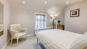 Een slaapkamer met een bed, een stoel, een nachtkastje, een lamp en een raam met zonwering.