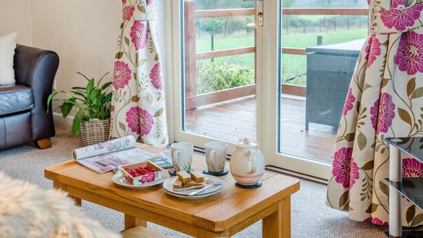 Un salón acogedor con una mesa de madera, un sofá y vistas a una terraza exterior a través de un ventanal.
