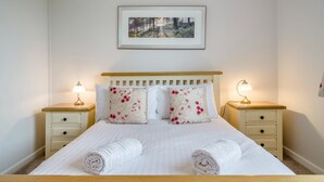Una cama bien hecha con dos almohadas, dos mesitas de noche con lámparas y un cuadro en la pared.