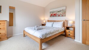 Una camera da letto con un letto in legno, due comodini con lampade, un comò in legno, uno specchio e un quadro appeso al muro.