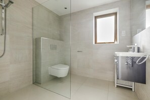 Ein modernes Badezimmer mit einer Glaskabine zur Dusche, einer Toilette und einem Waschbecken mit Handtuchhalter.