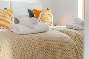 Ein Hotelzimmer mit ordentlich gefalteten Handtüchern auf dem Bett, einer gemusterten Tagesdecke und zwei Kissen mit Fransenbesatz.