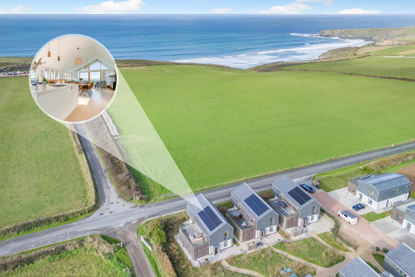 An aerial view of a coastal residential area with houses, a road, and a large green field.