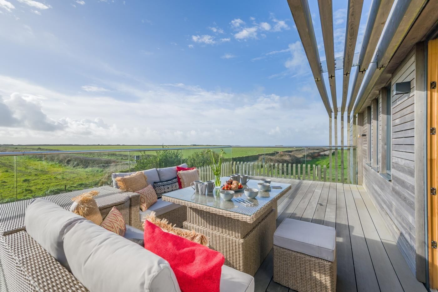 Een balkon met rieten meubels, een gedekte tafel en uitzicht op een groen landschap.