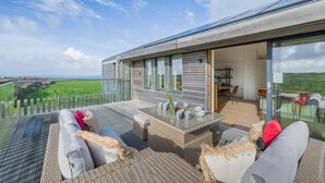 A modern outdoor living space with a glass wall, wicker furniture, and a view of the countryside. - 3 Bed in St. Eval (oc-s32502) (Saint Eval)