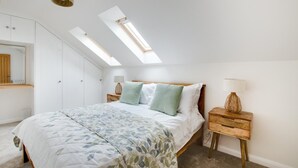 Ein Schlafzimmer mit einer Dachfensterkuppel, einem Bett mit floralem Überwurf, einem hölzernen Nachttisch und einem Spiegel.