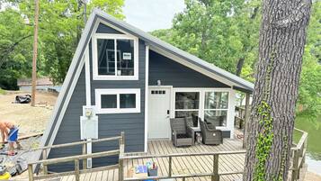 Une cabane à deux étages dotée d’une terrasse, de grandes fenêtres et d’une porte donnant sur l’intérieur.