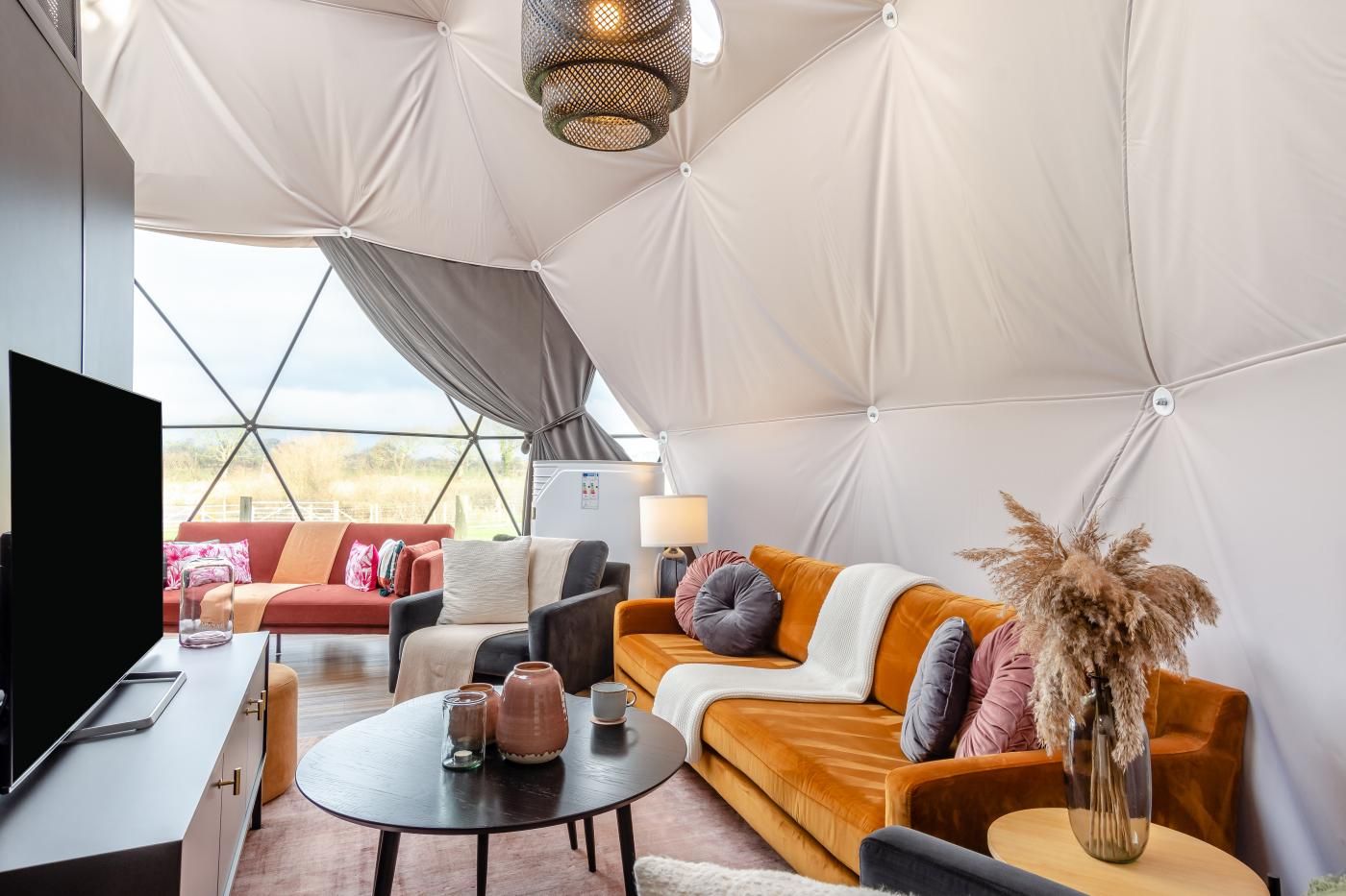 A spacious tented room with a sofa, chairs, a table, and a TV.