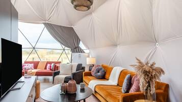 A spacious tented room with a sofa, chairs, a table, and a TV.