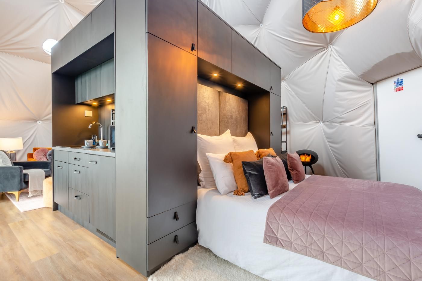 A compact room with a bed, bedside table, and a built-in kitchenette.
