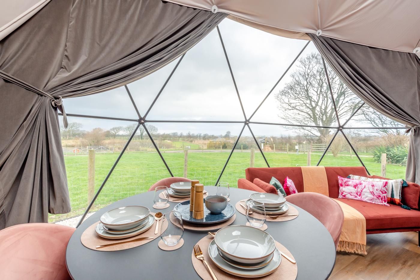 A tented dining area with a table set for four, a sofa, and a view of the countryside.